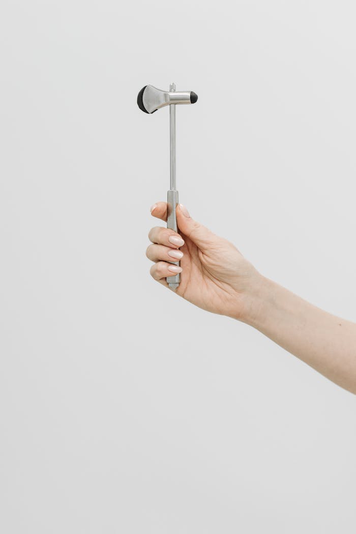 Close-up of a hand holding a stainless steel reflex hammer against a neutral background.